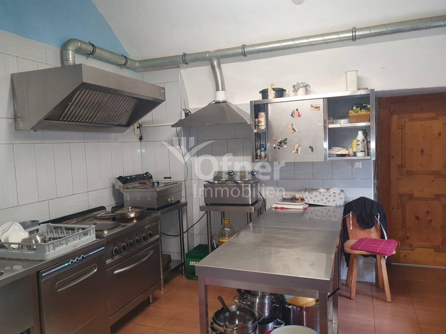 Professionelle Gastroküche mit Edelstahloberflächen, Dunstabzugshauben und Fliesenwänden.