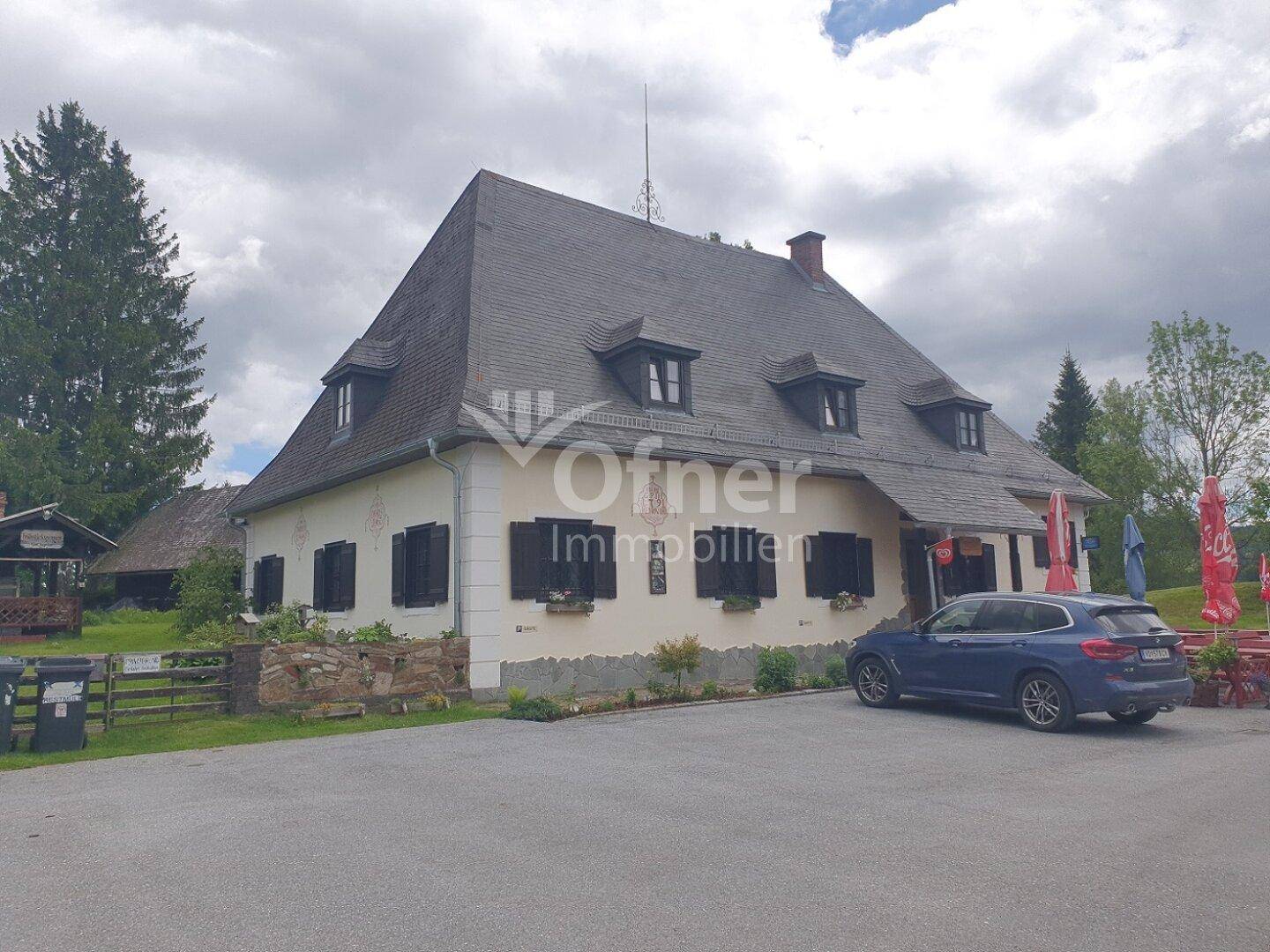 Rückansicht des Landgasthofs mit Parkplatz und umliegender grüner Landschaft.