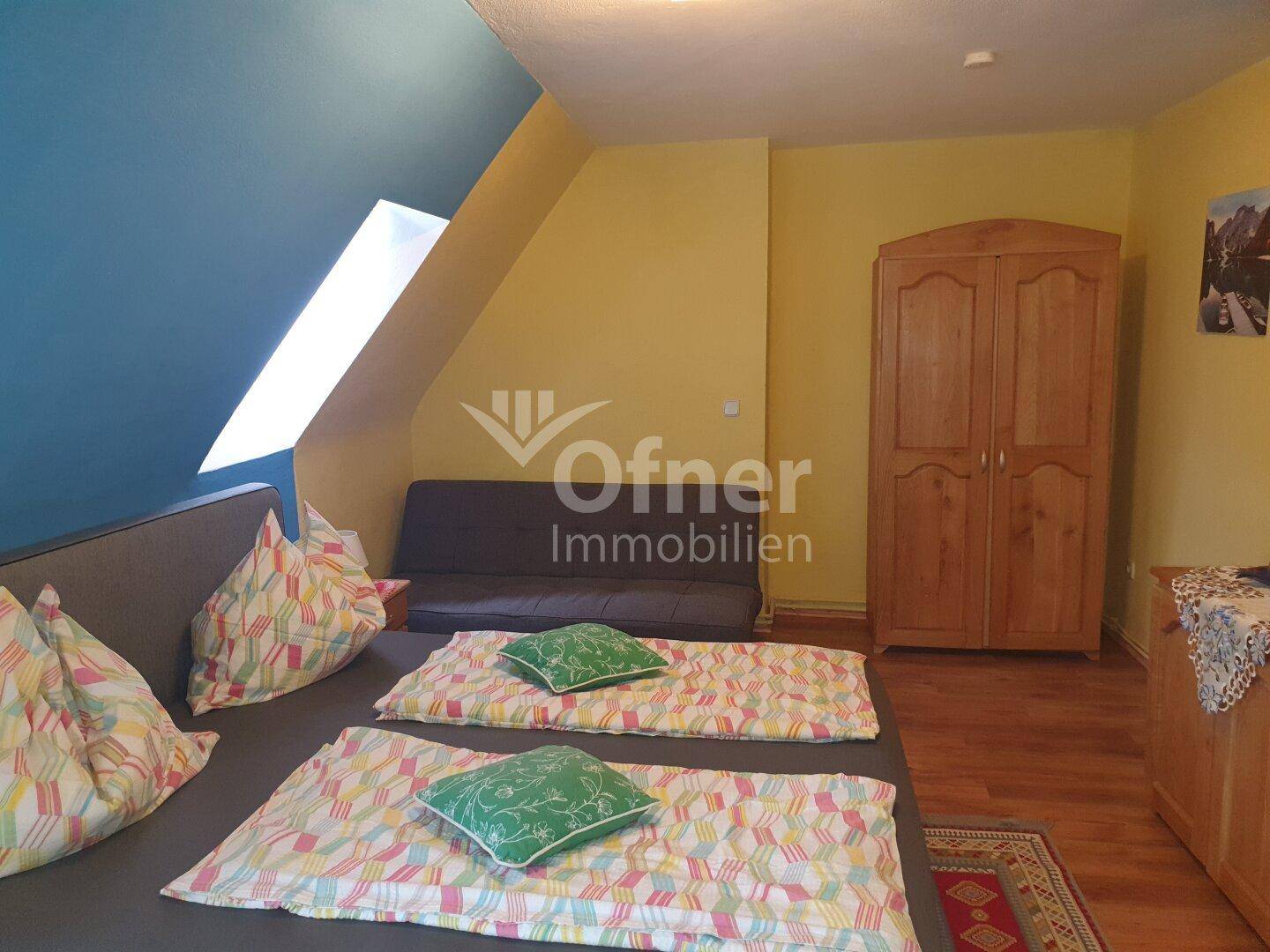 Gemütliches Schlafzimmer im Dachgeschoss mit Holzboden, Dachfenster und blauer Wand.