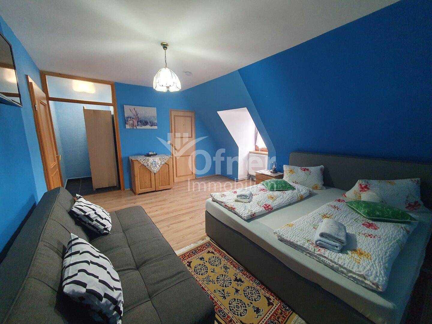 Geräumiges Schlafzimmer mit blauer Akzentwand, Holzboden und bequemen Betten.