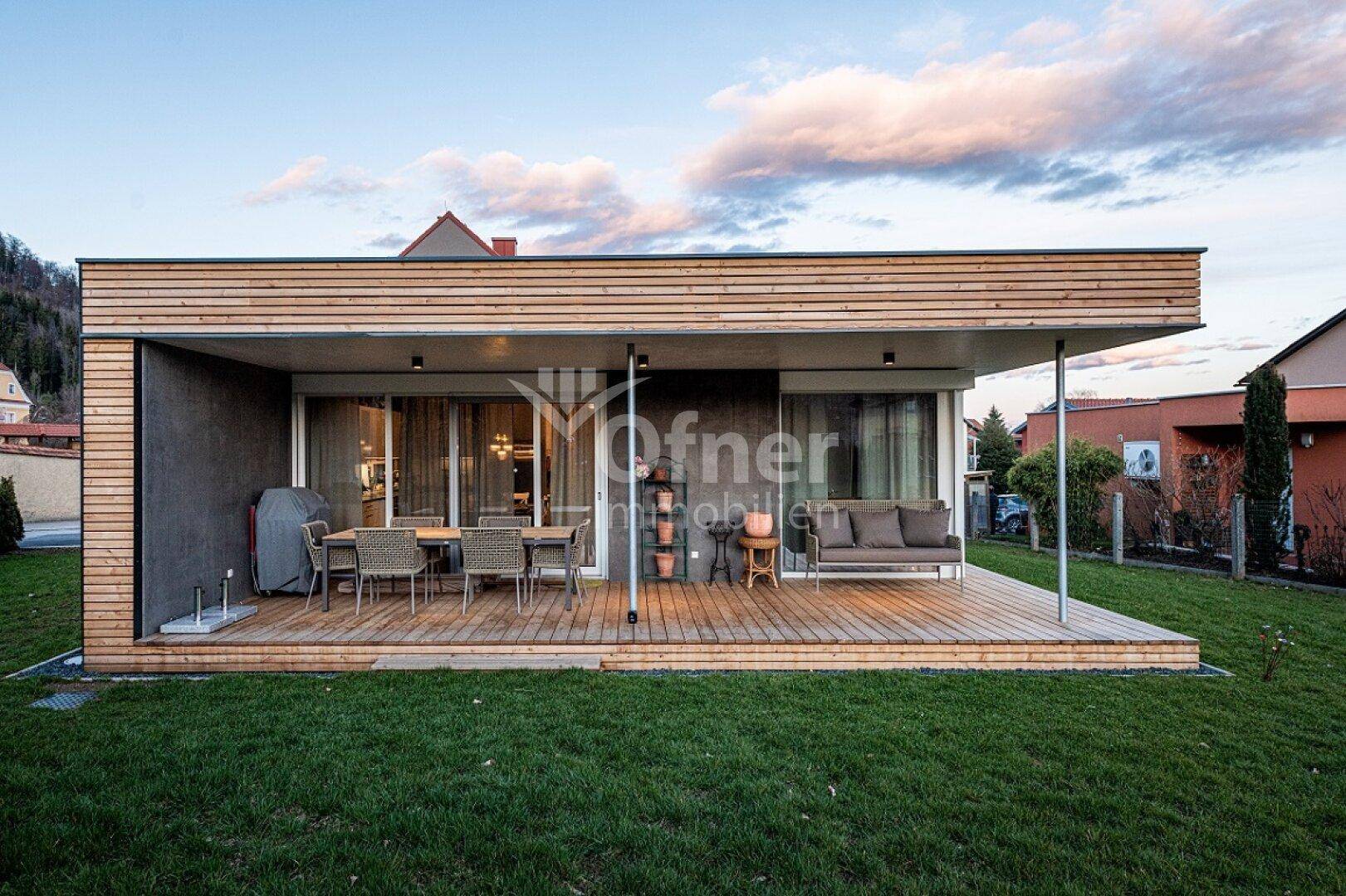 Großzügige Holzterrasse mit Ess- und Lounge-Bereich, umgeben von einem grünen Garten.