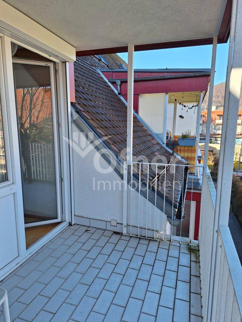 Überdachter Balkon mit Fliesenboden und Blick auf die umliegenden Dächer und Berge.