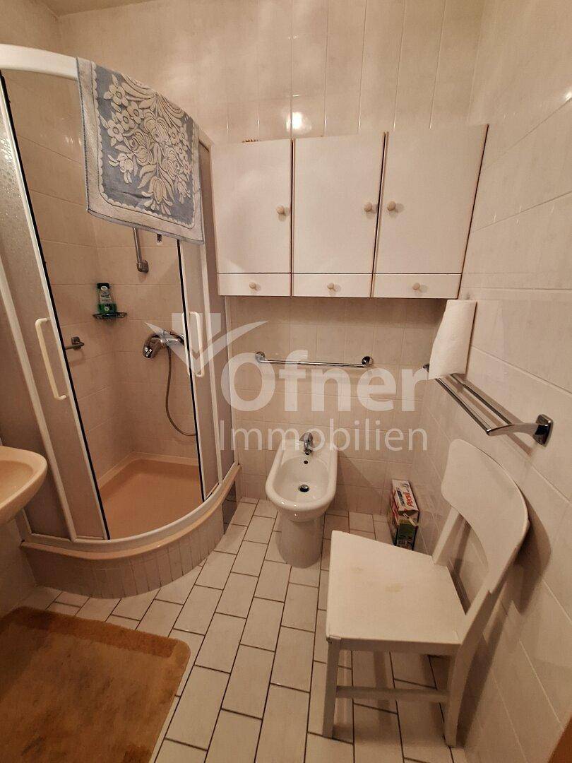 Badezimmer mit Duschkabine, Bidet und weißen Wand- und Bodenfliesen, sauber und gepflegt.