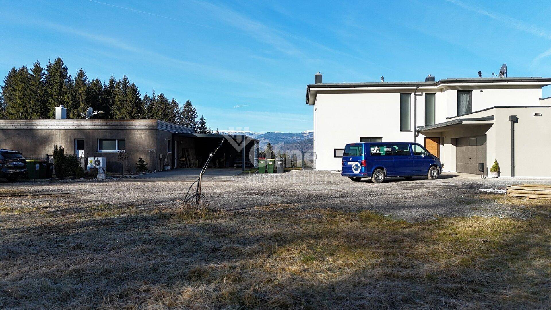 Ansicht des modernen Wohnhauses mit Nebengebäude und geparkten Fahrzeugen auf dem Grundstück.
