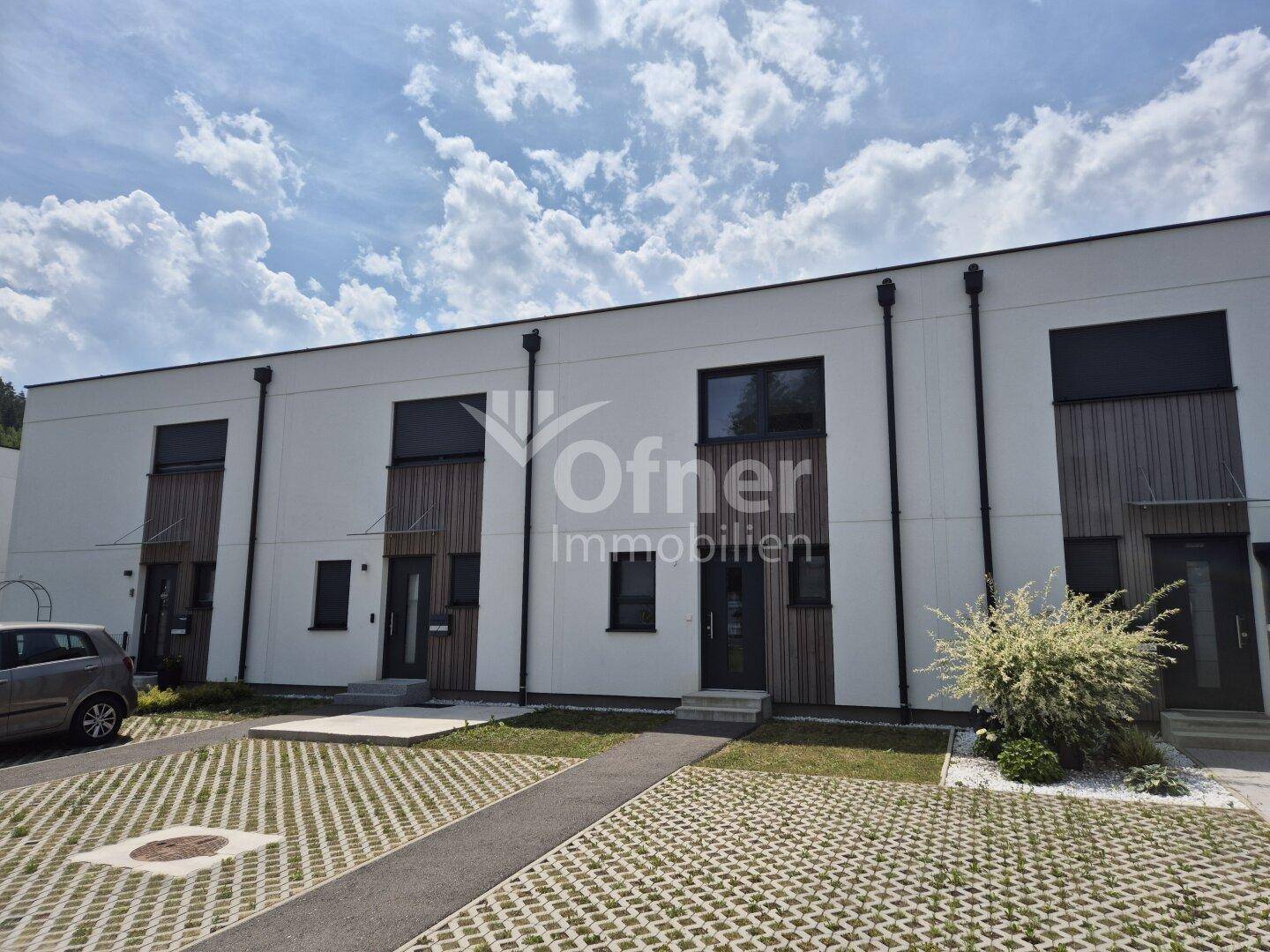 Moderne Reihenhäuser mit weißer Fassade, dunklen Fenstern und gepflasterten Parkflächen.