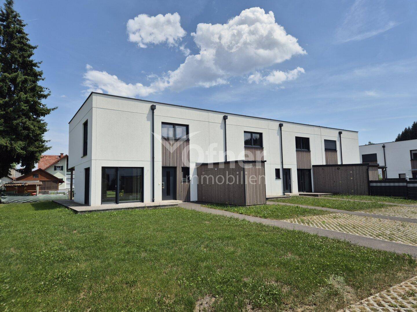 Reihenhäuser mit moderner Architektur, weißer Fassade und Holzverkleidung, umgeben von Grünflächen.