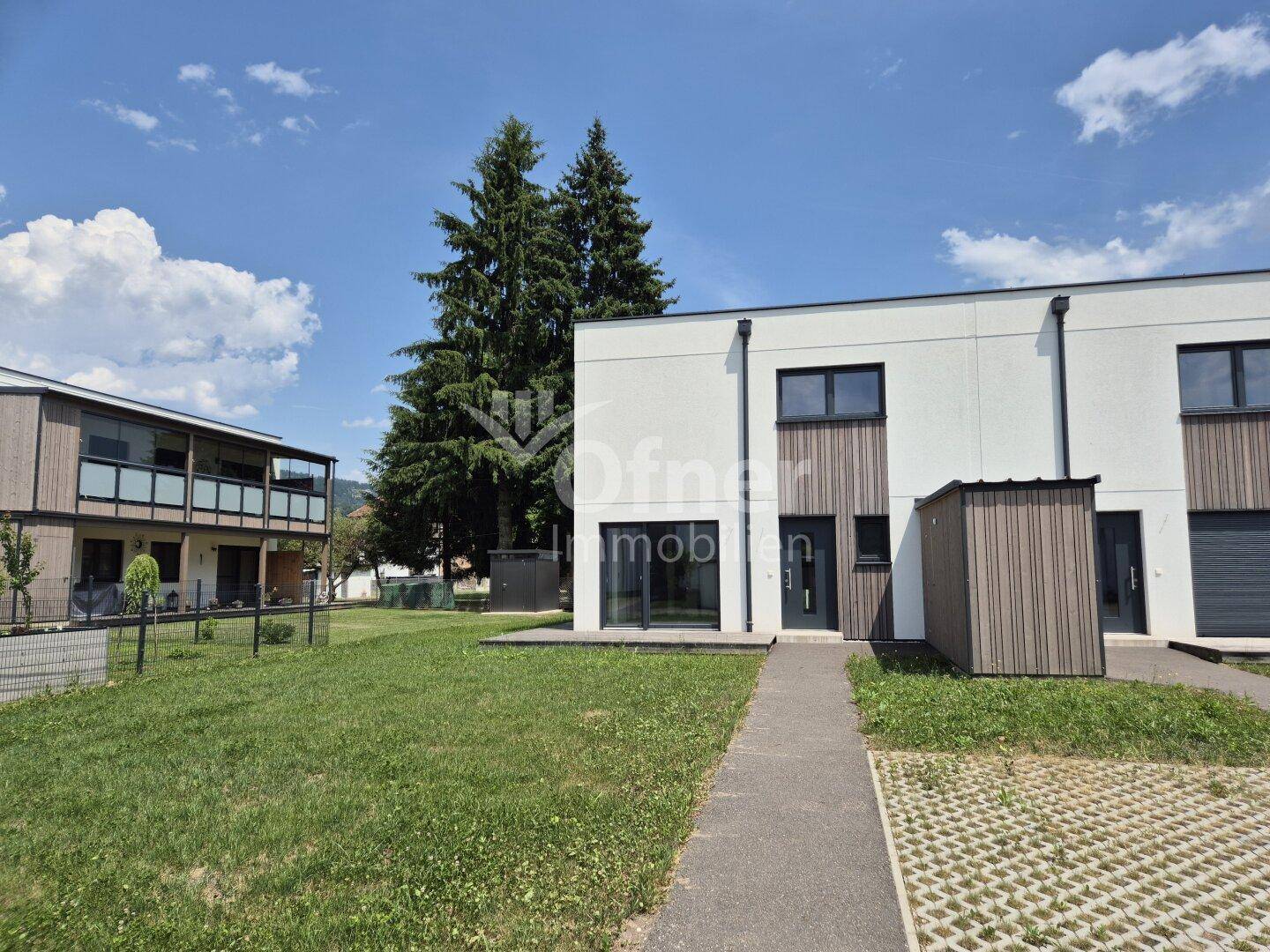 Vorderansicht eines modernen Reihenhauses mit weißer Fassade, Holzdetails und gepflastertem Zugang.