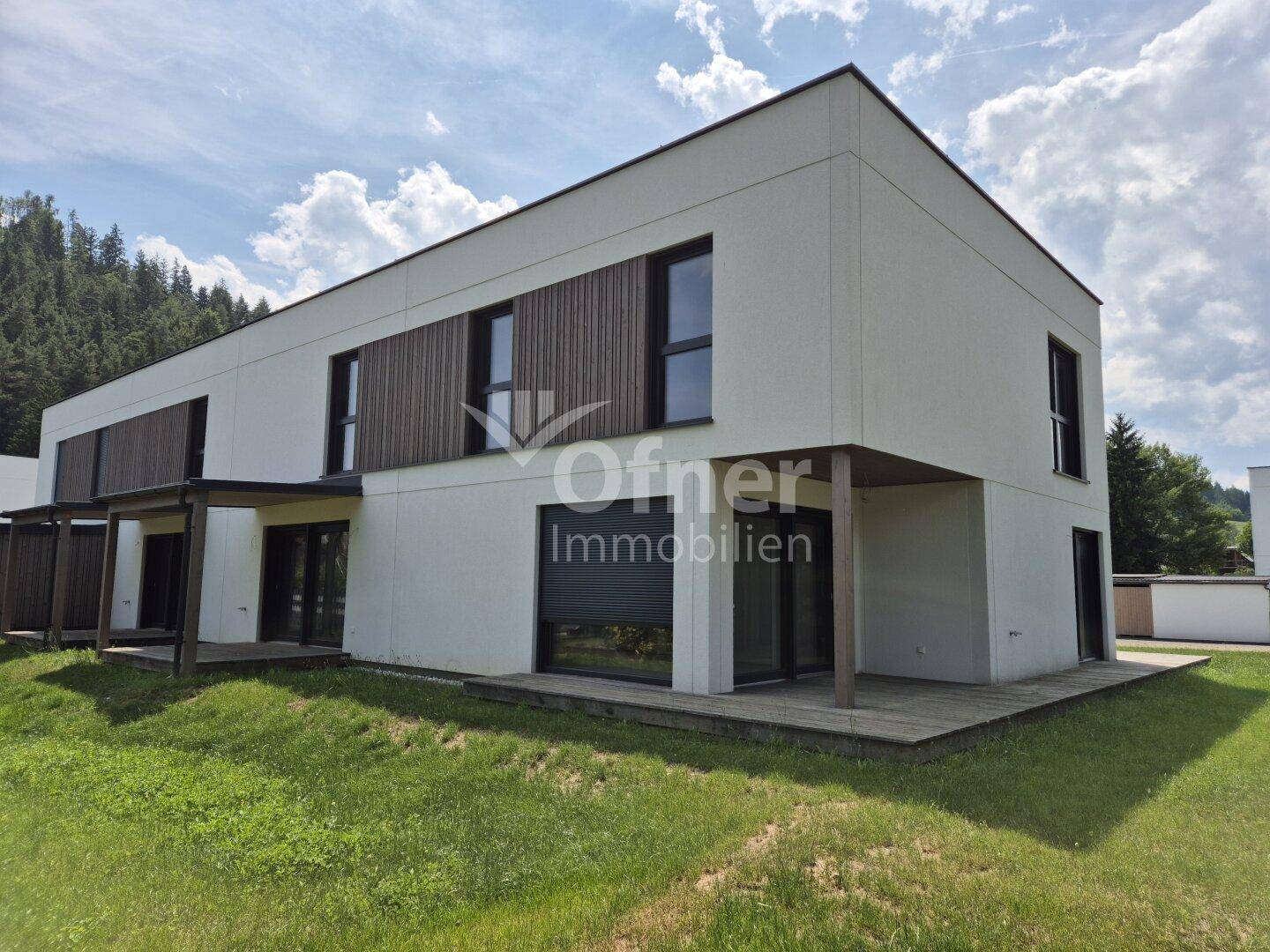 Modernes Reihenhaus mit weißer Fassade, Holzdetails und einer Holzterrasse im Gartenbereich.