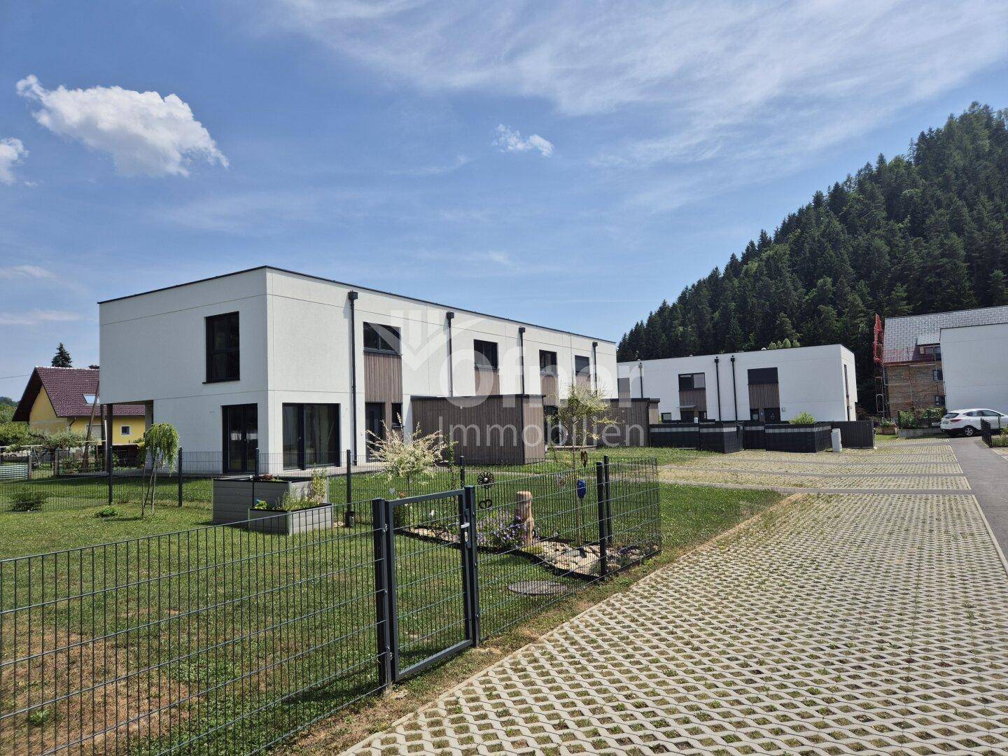 Moderne Reihenhäuser mit weißer Fassade und Blick auf bewaldete Hügel unter blauem Himmel.