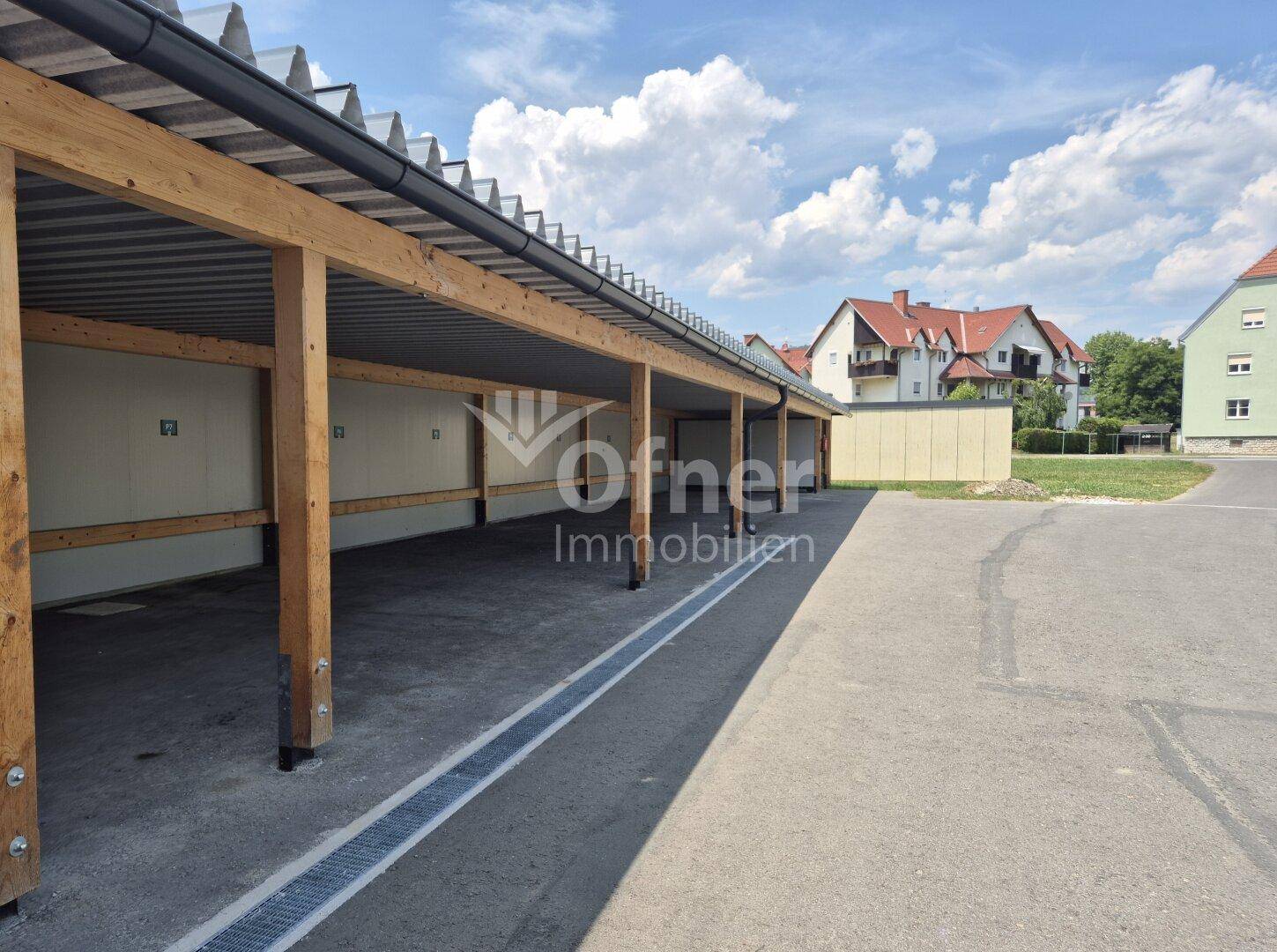 Überdachte Parkplätze in einem Carport mit Holzkonstruktion und Wellblechdach.