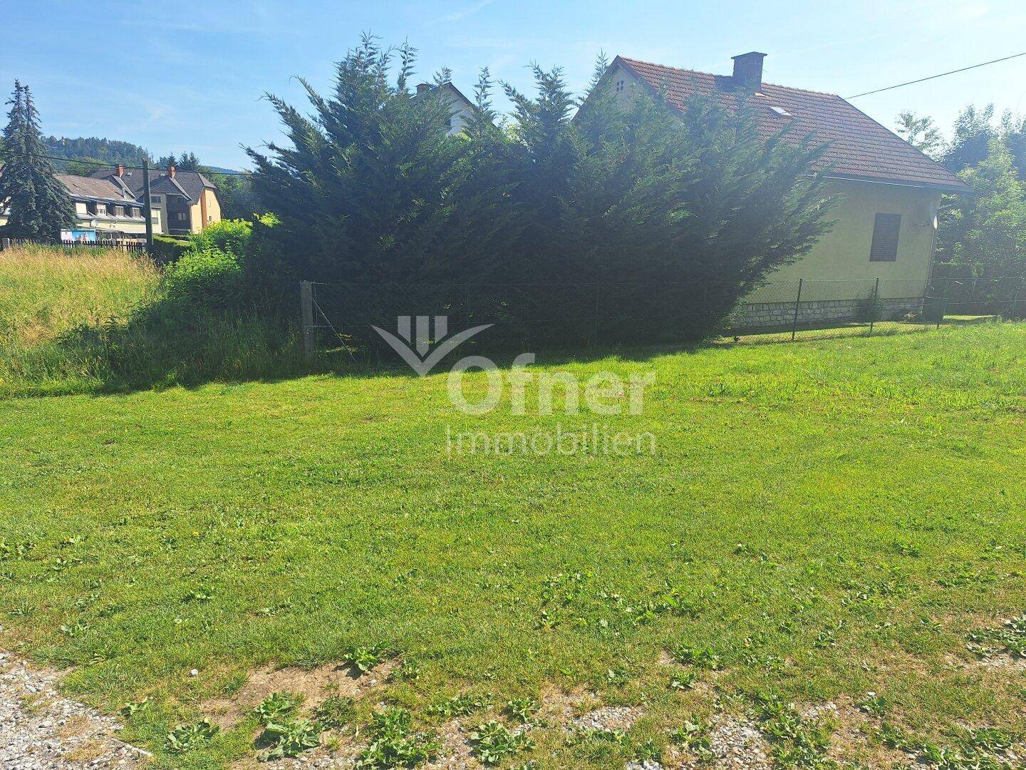 Haus mit gelber Fassade und rotem Dach, umgeben von einer großen Rasenfläche und Bäumen.