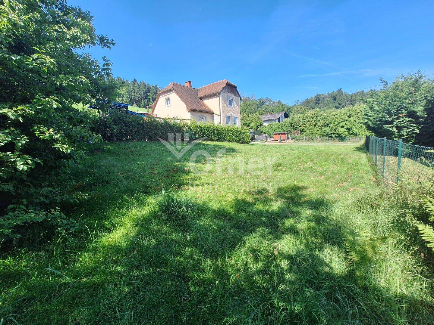 Weitläufiges Grundstück mit grüner Wiese und einem traditionellen Haus im Hintergrund, umgeben von Natur.