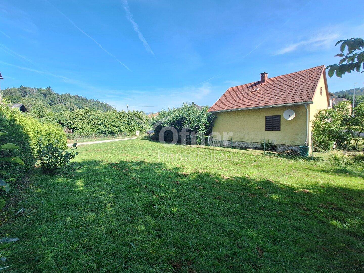 Seitenansicht eines Hauses mit gelber Fassade und rotem Dach, umgeben von einer grünen Rasenfläche.