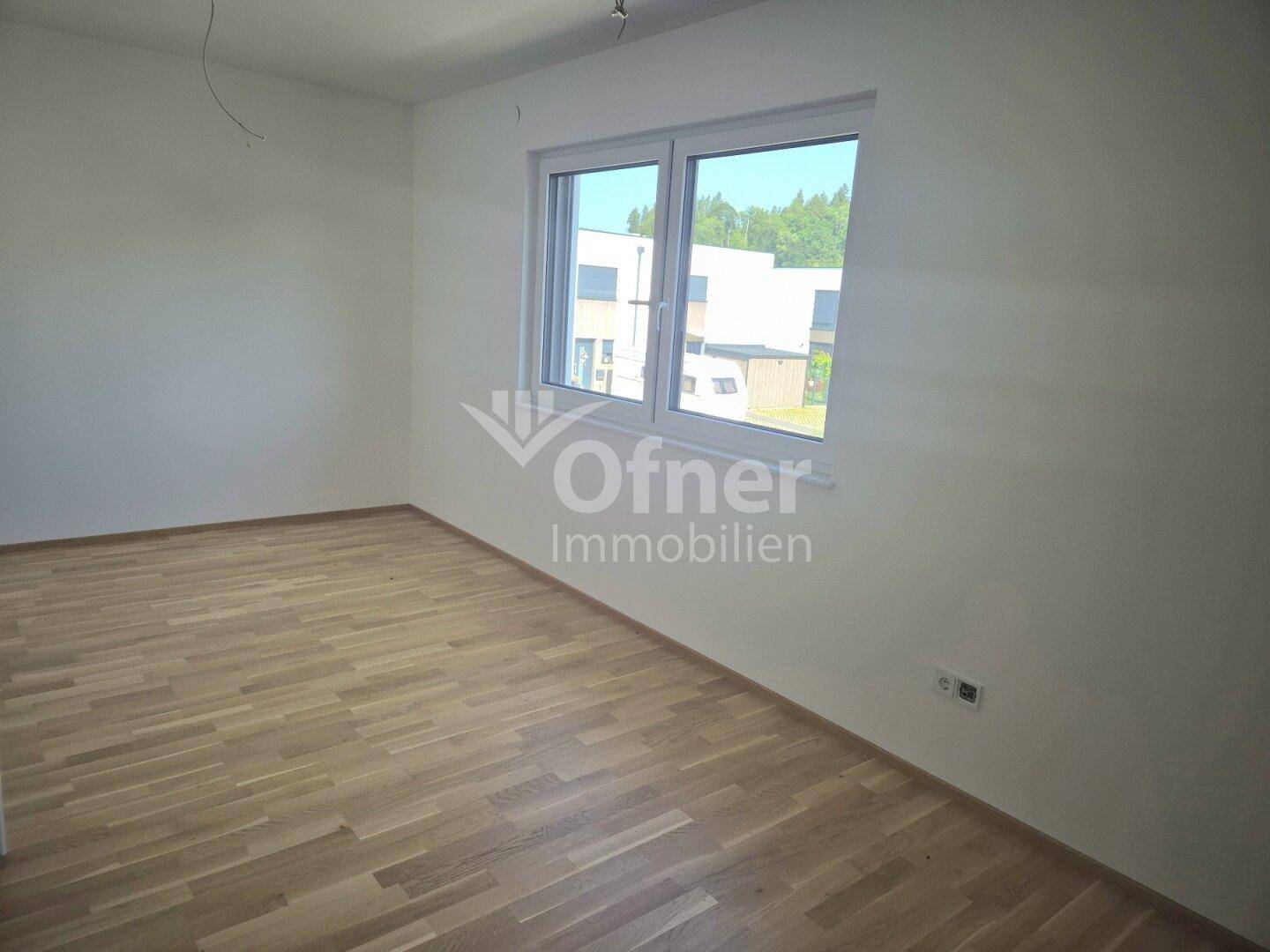 Helles Schlafzimmer mit Parkettboden und großem Fenster, das viel Tageslicht hereinlässt.