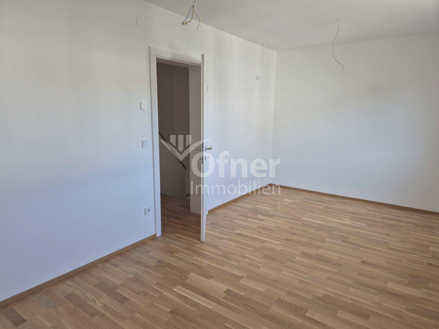 Leeres Zimmer mit Parkettboden und weiß gestrichenen Wänden, ideal als Schlaf- oder Arbeitszimmer.