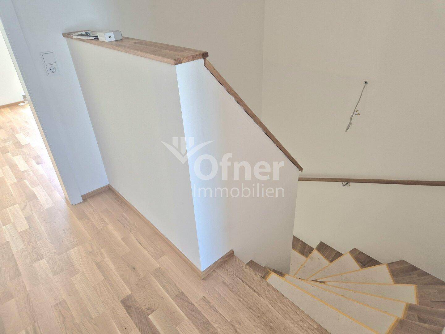 Treppenaufgang mit Holzstufen und weißem Geländer, verbindet die verschiedenen Wohnebenen.