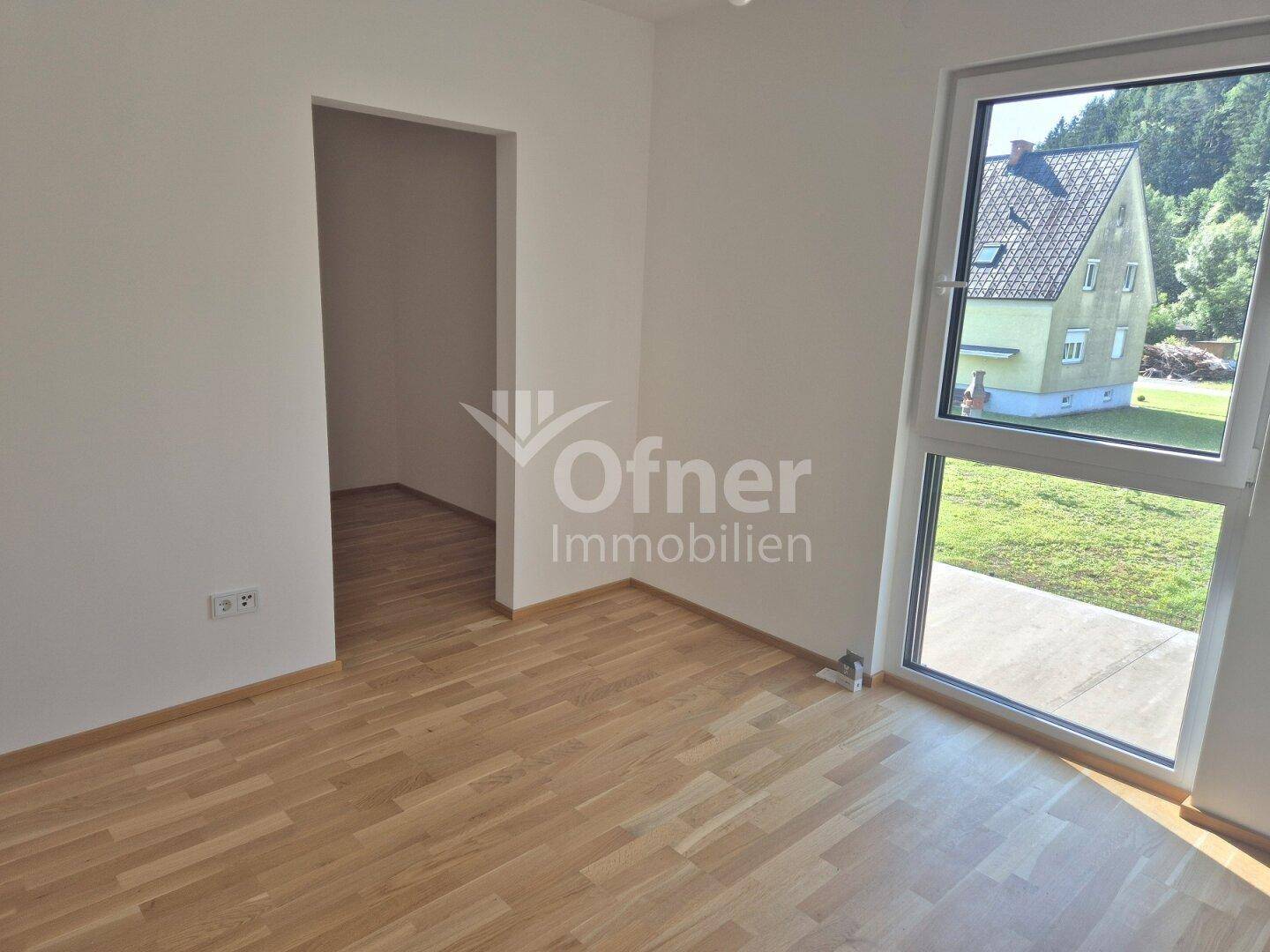 Helles Zimmer mit Parkettboden und großem Fenster, bietet Blick ins Grüne.