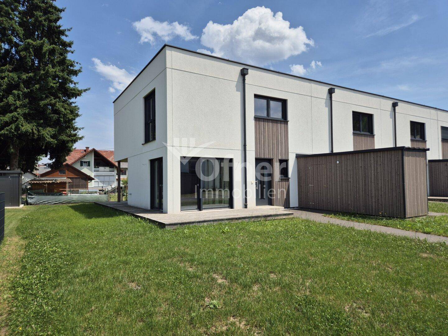 Rückseite eines modernen Reihenhauses mit kleiner Holzterrasse und Rasenfläche.