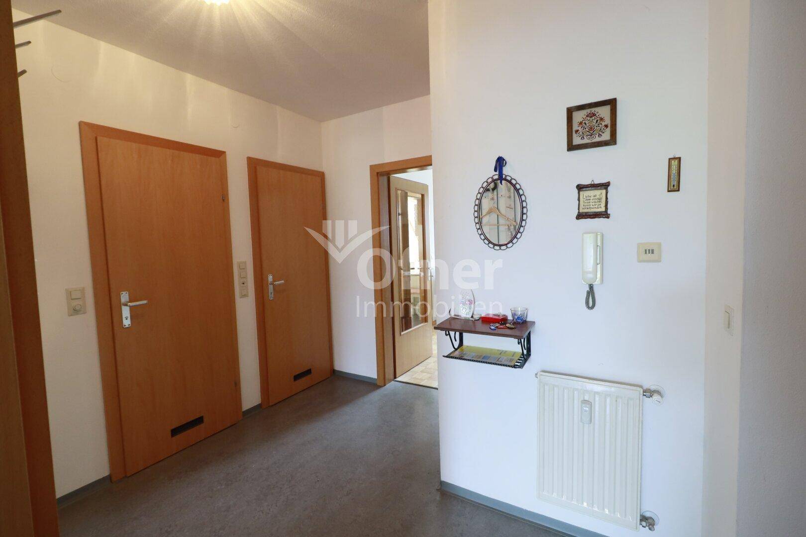 Heller Flur mit Holztüren, Garderobe und einem Heizkörper, der zu weiteren Räumen führt.