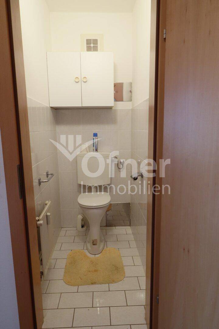 Separate Toilette mit WC, kleinem Waschbecken und weißen Fliesen, funktional und hell.