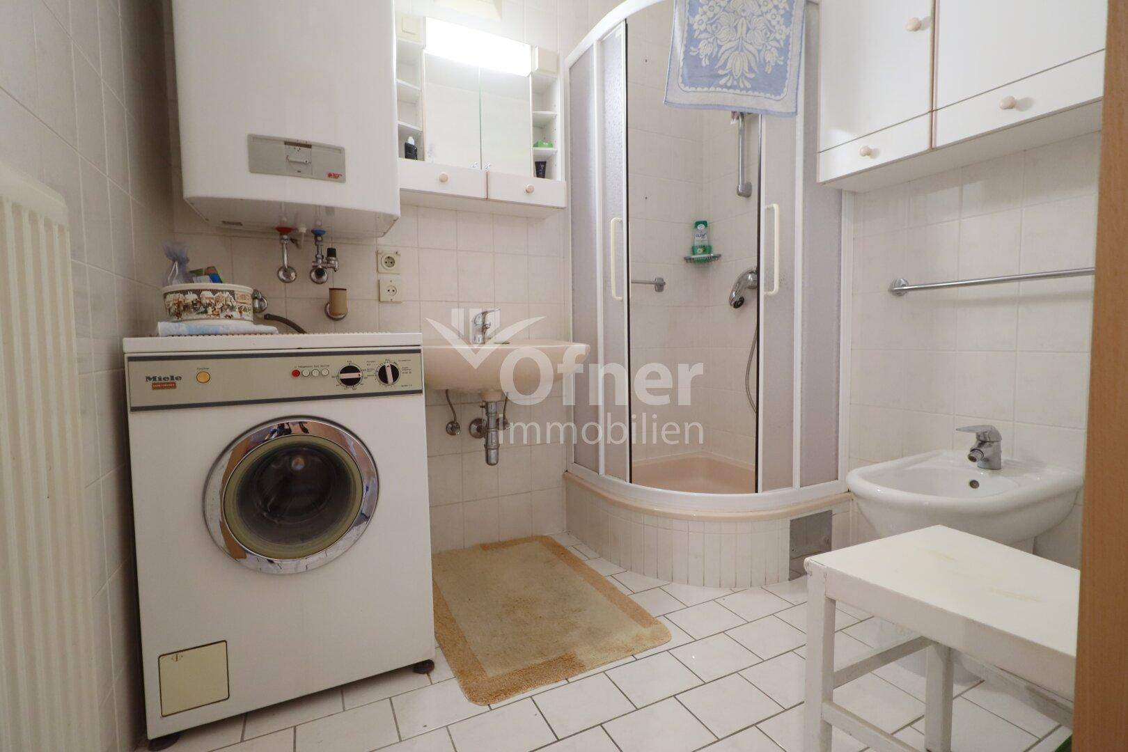 Badezimmer mit Dusche, Waschmaschine, Bidet und weißen Fliesen, funktional eingerichtet.