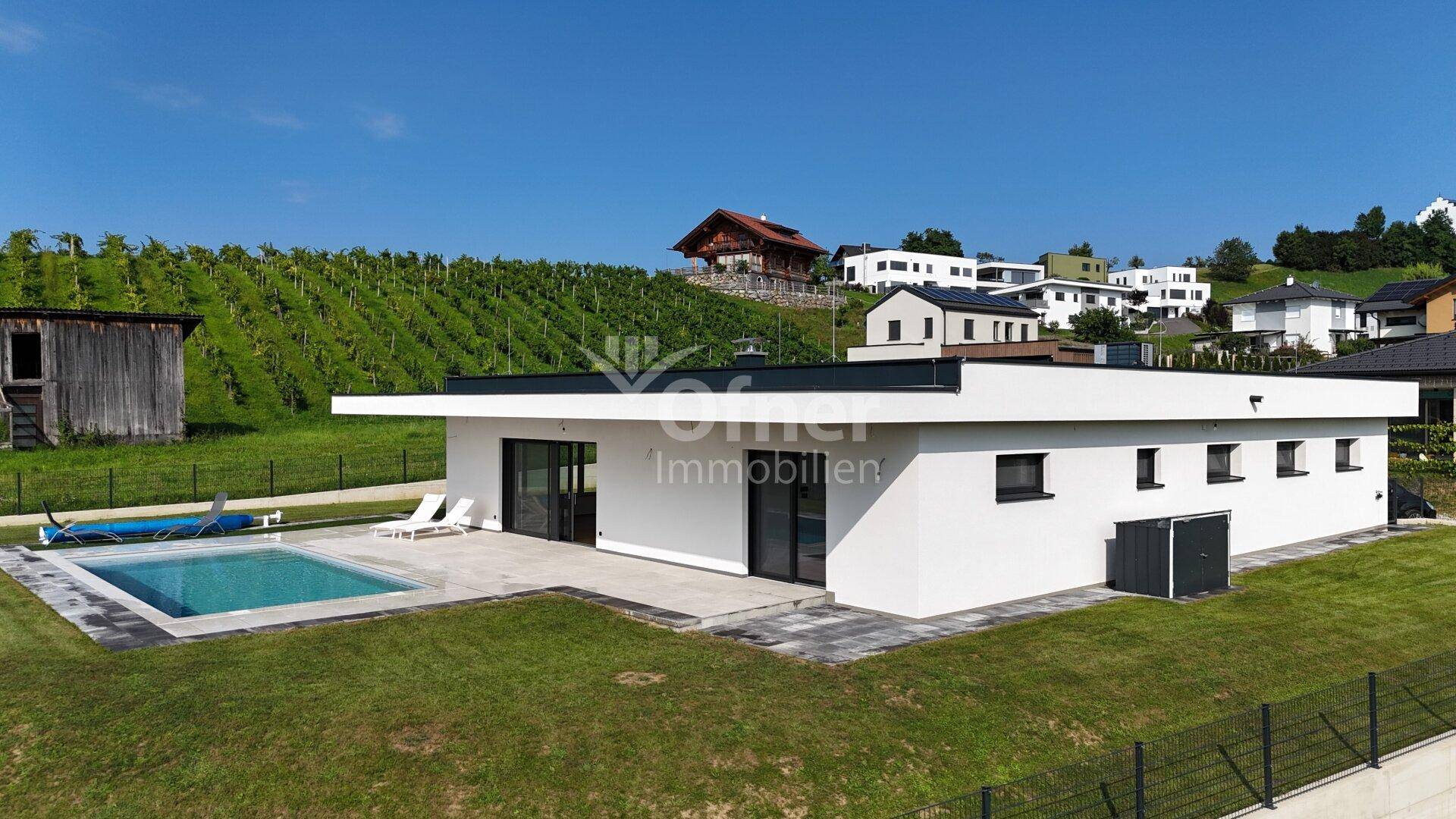 Moderne Villa mit Pool und Terrasse unter blauem Himmel, umgeben von grünen Weinbergen.