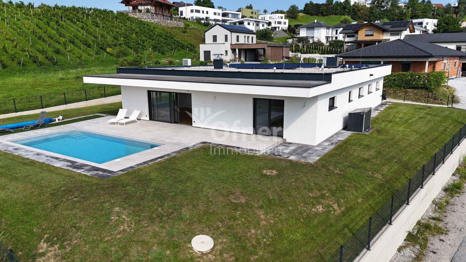 Ansicht der modernen Villa mit Pool, Terrasse und angrenzendem Weinberg im Hintergrund.
