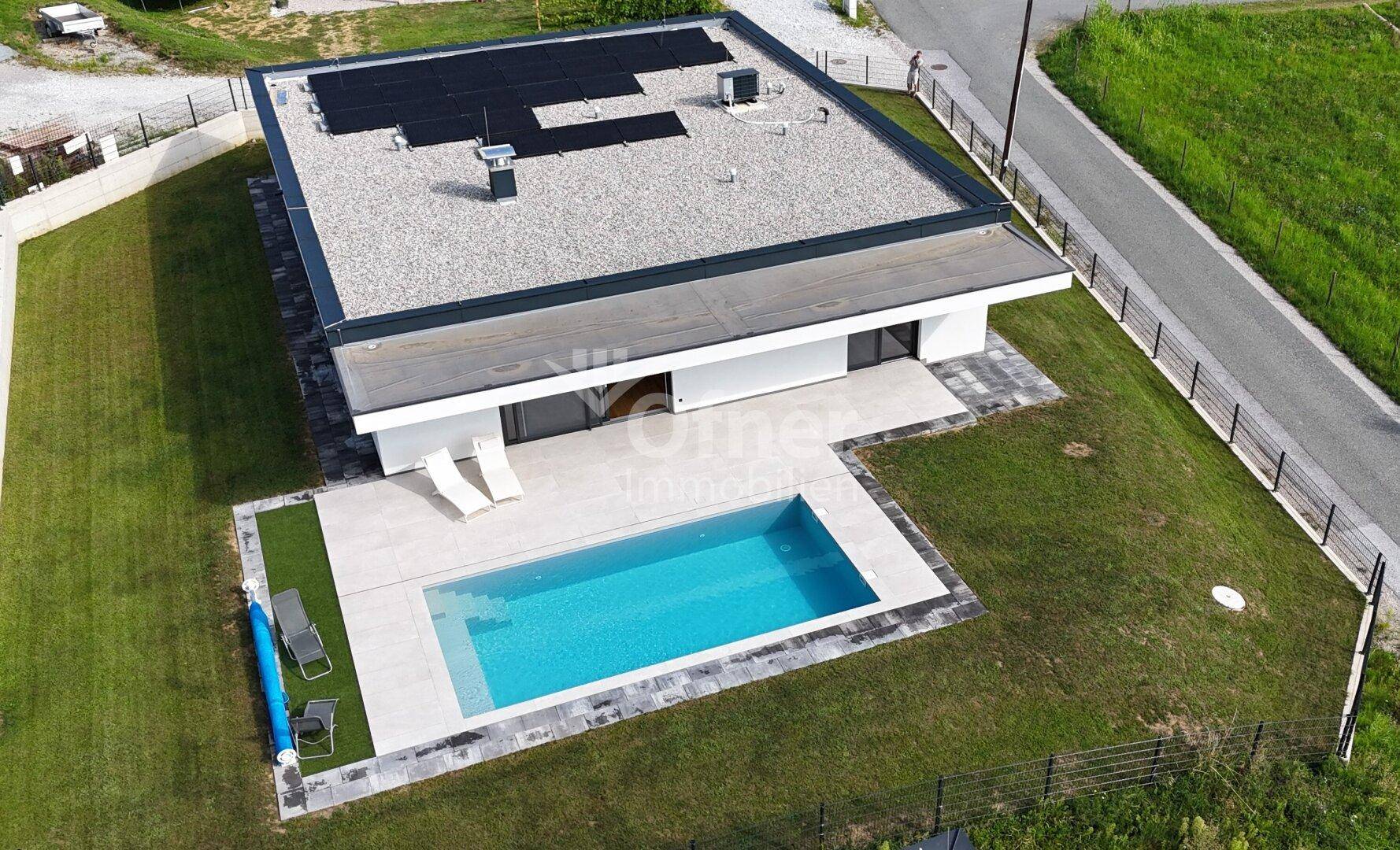 Vogelperspektive der modernen Villa mit Flachdach, Solaranlage und großzügigem Poolbereich.