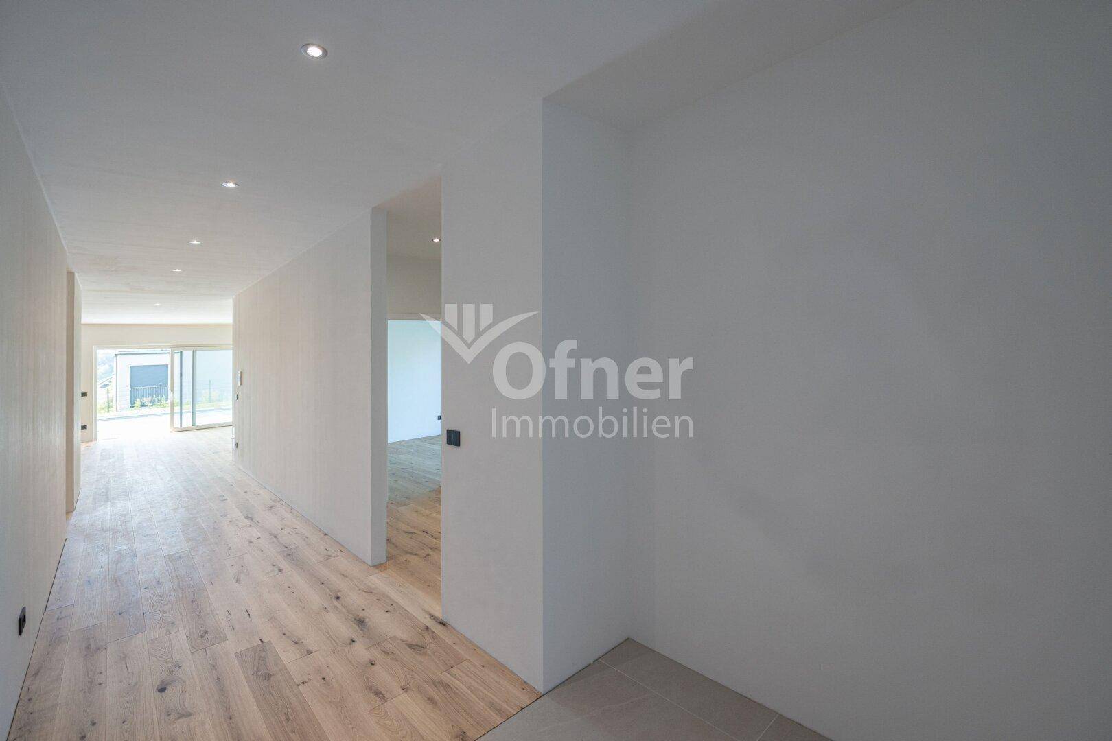 Langer, heller Flur mit Holzboden und Zugang zu einem lichtdurchfluteten Wohnbereich.
