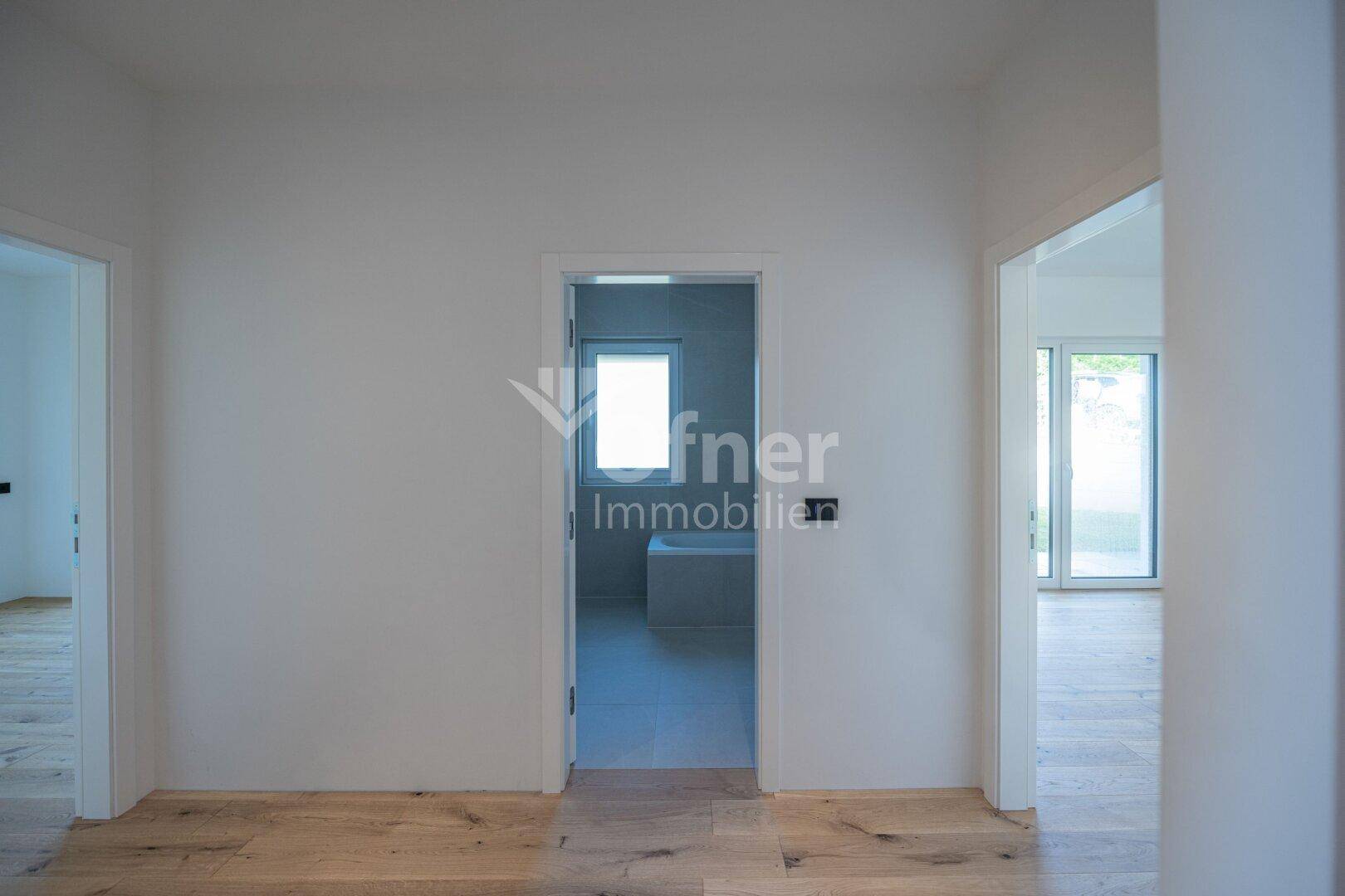 Flur mit Holzboden und Blick in ein modernes Badezimmer mit hellen Fliesen.