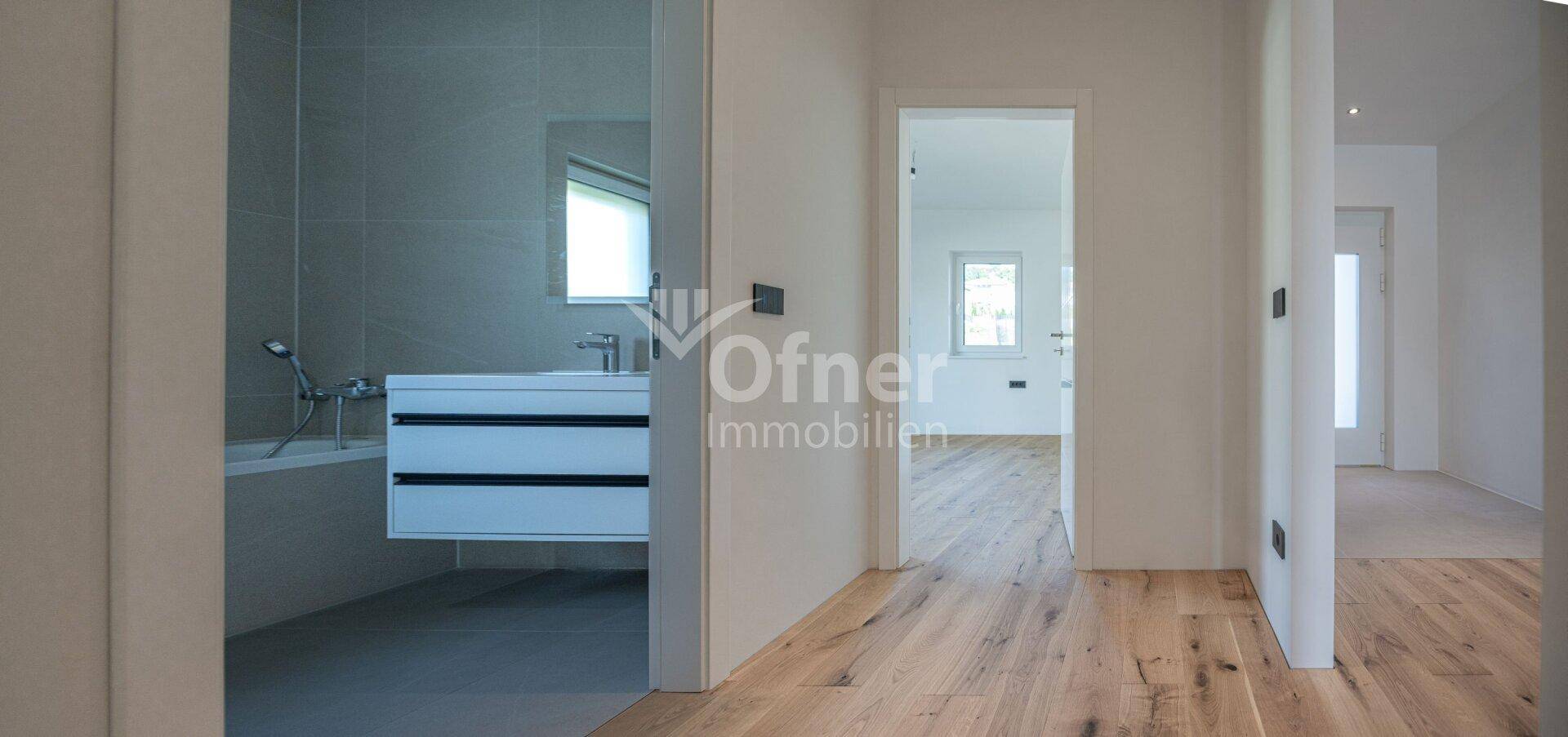 Modernes Badezimmer mit Waschtisch, Badewanne und hellen Fliesen, zugänglich vom Flur.