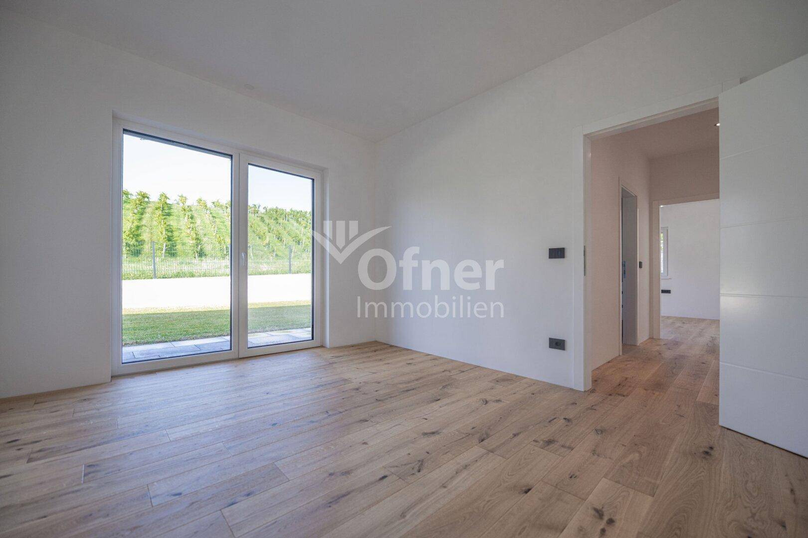 Geräumiger, heller Raum mit Holzboden und großen Fenstern, die viel Tageslicht hereinlassen.
