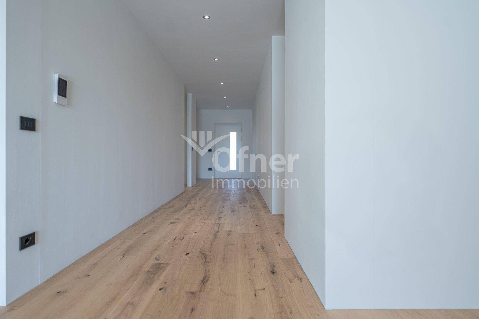 Langer, minimalistischer Flur mit hellem Holzboden und weiß gestrichenen Wänden.