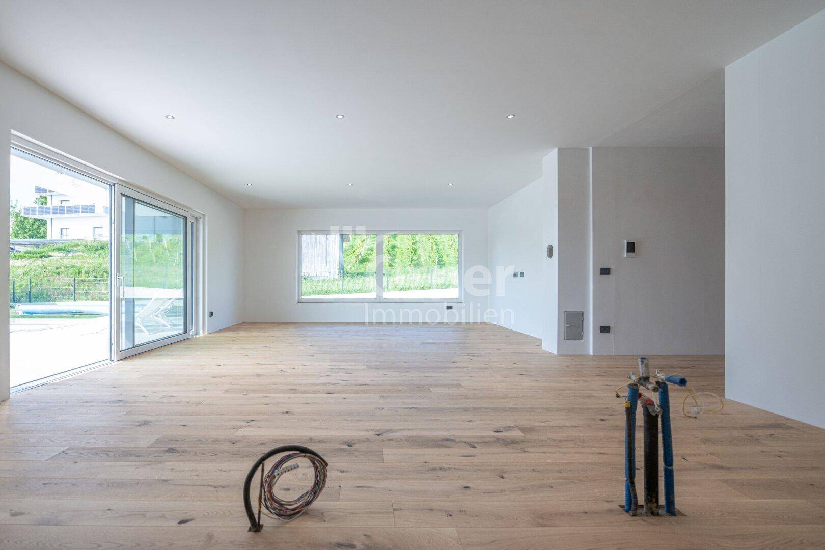 Großer, offener Wohnbereich mit Holzboden und weiten Fensterfronten, die zum Poolbereich führen.