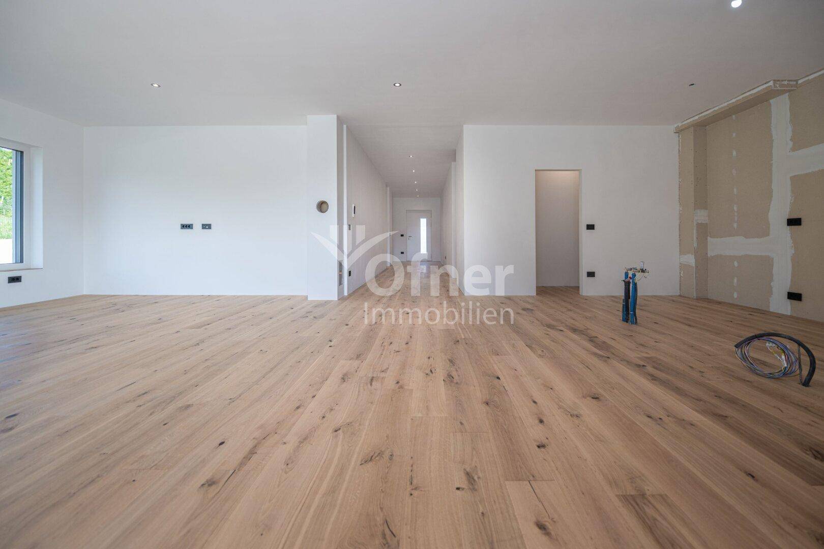 Geräumiger, offener Wohnbereich mit Holzboden und Zugang zum Flur, bereit für die Einrichtung.