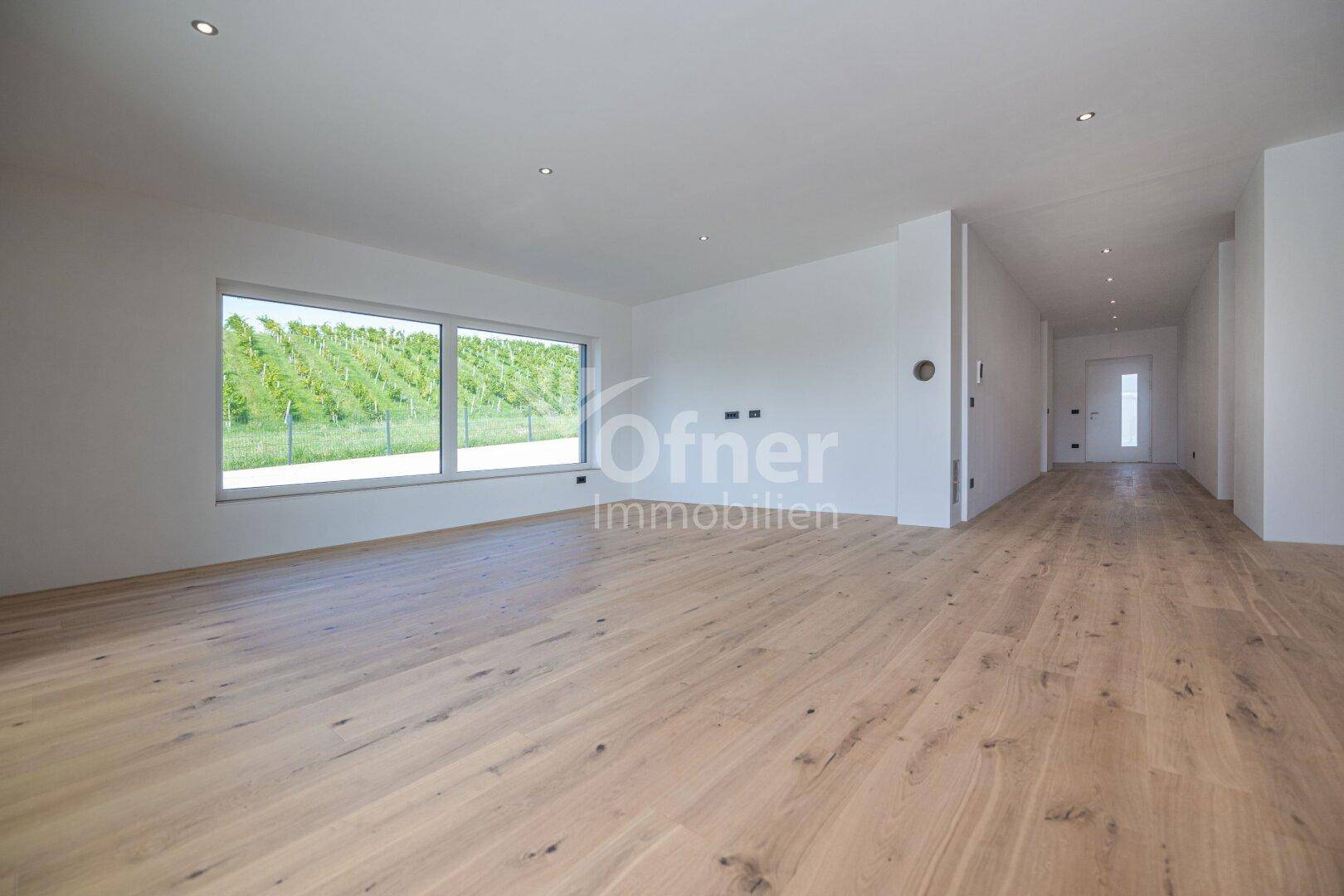 Weitläufiger, offener Wohnbereich mit Holzboden, großen Fenstern und Zugang zum Eingangsbereich.