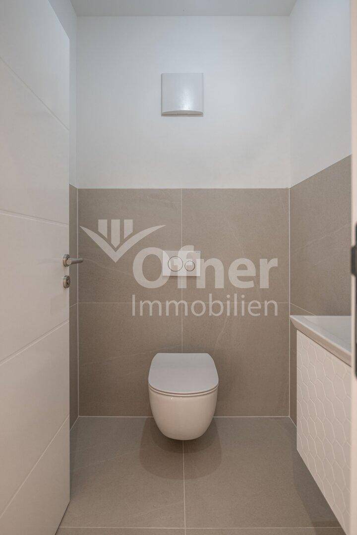 Modernes Gäste-WC mit wandhängender Toilette und hellgrauen Fliesen an Wänden und Boden.