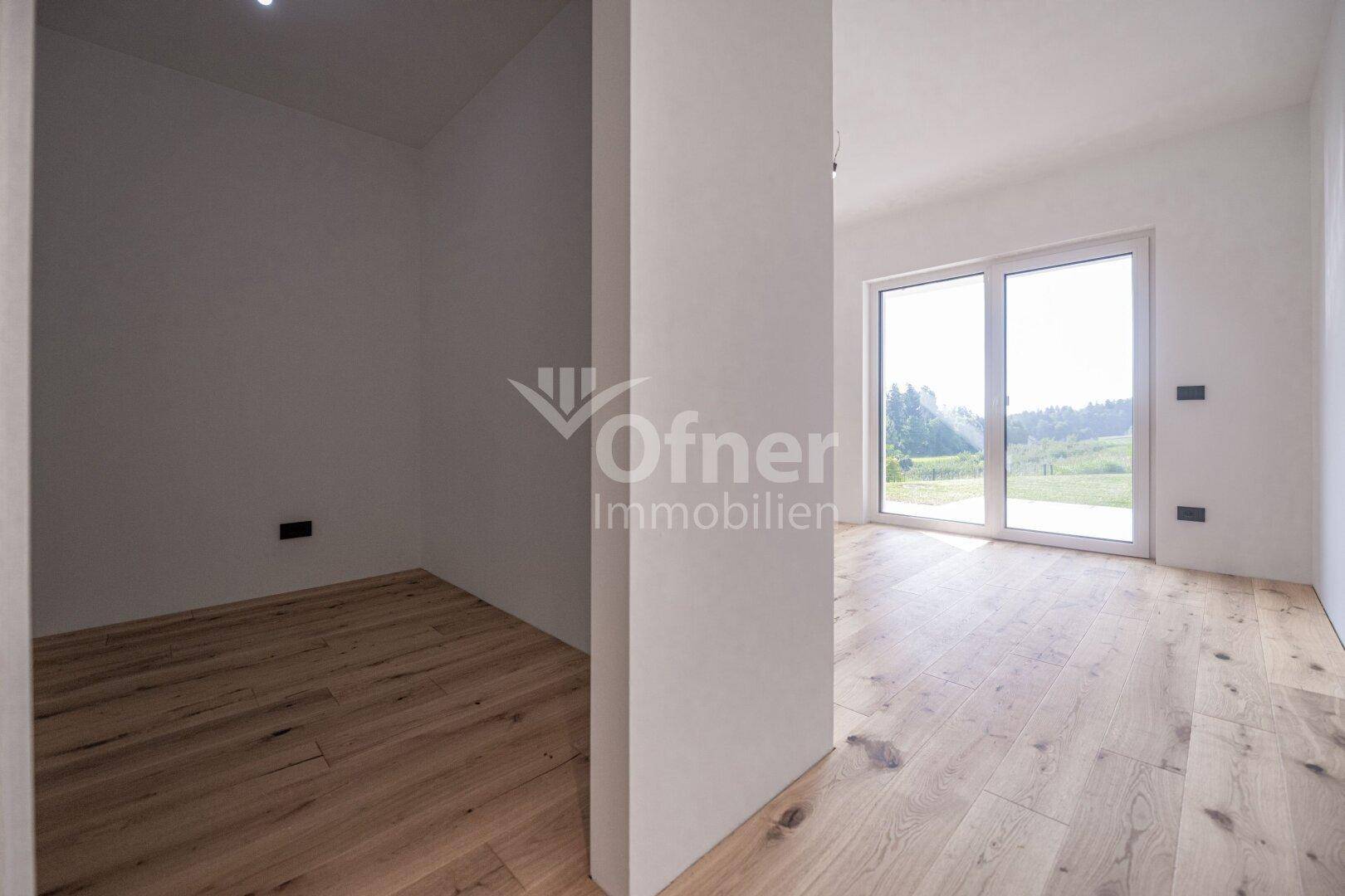 Heller Raum mit Holzboden, großen Schiebetüren und einem angrenzenden Abstellbereich.