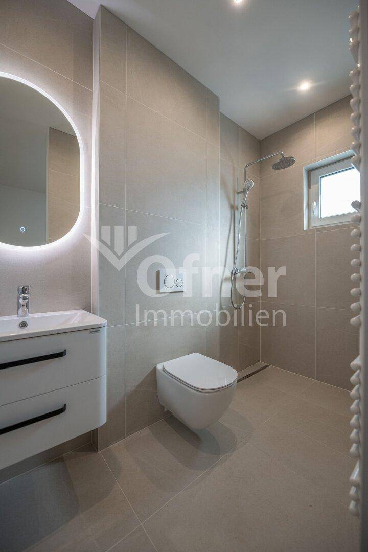 Modernes Badezimmer mit ebenerdiger Dusche, Waschtisch, Toilette und beheiztem Handtuchhalter.
