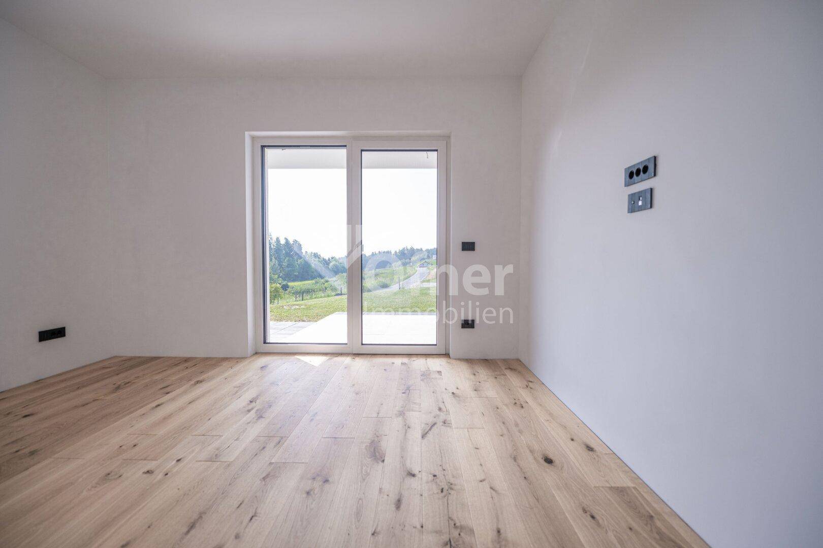 Leerer Raum mit Holzboden und einer großen Glasschiebetür, die ins Freie führt.