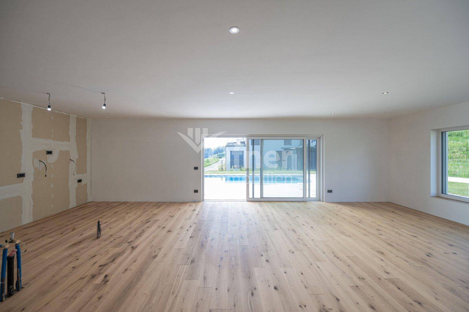 Geräumiger Wohnbereich mit Holzboden und großen Schiebetüren zum Poolbereich.
