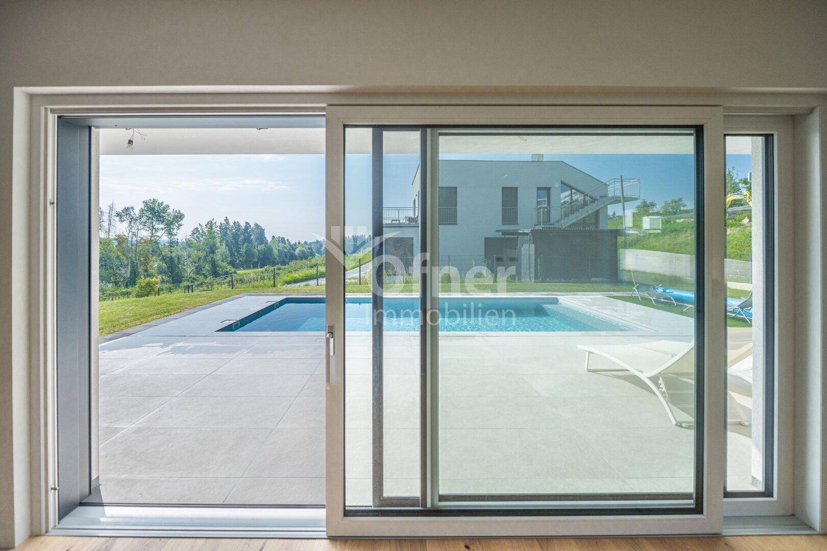 Große Glasschiebetür, die den Blick auf den Außenbereich mit Pool und moderner Architektur freigibt.