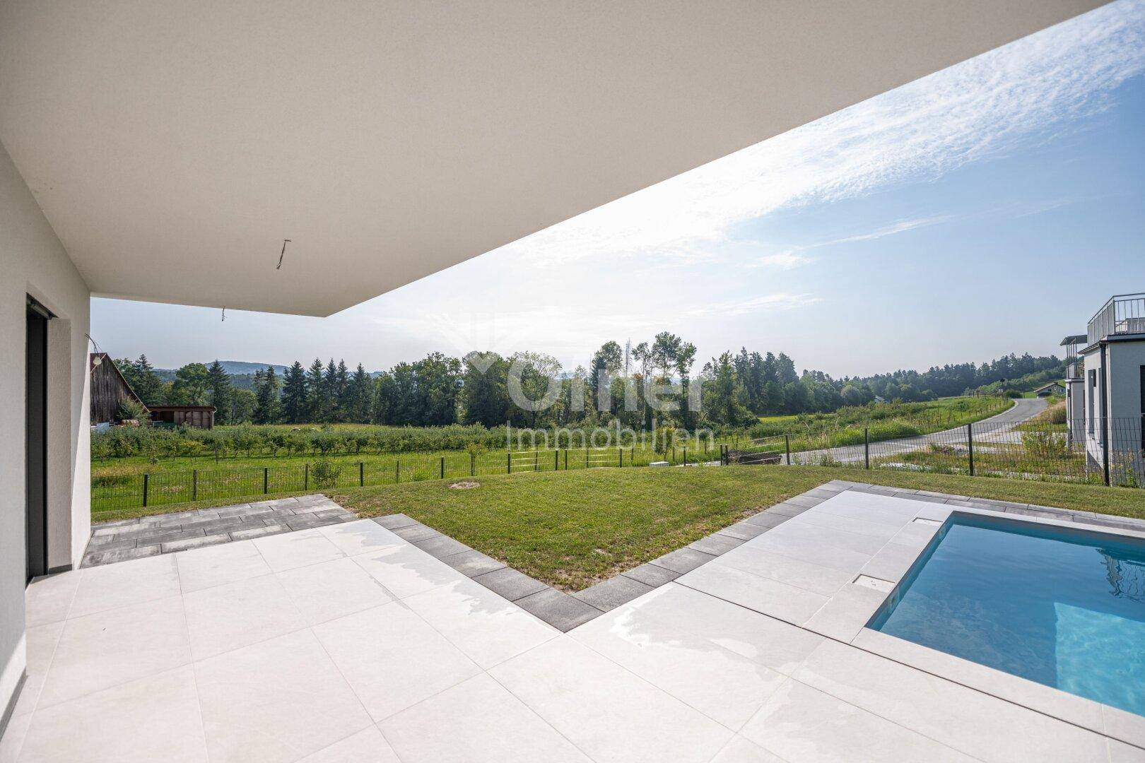 Sonniger Terrassenbereich mit Pool und weitem Blick auf die grüne Landschaft.