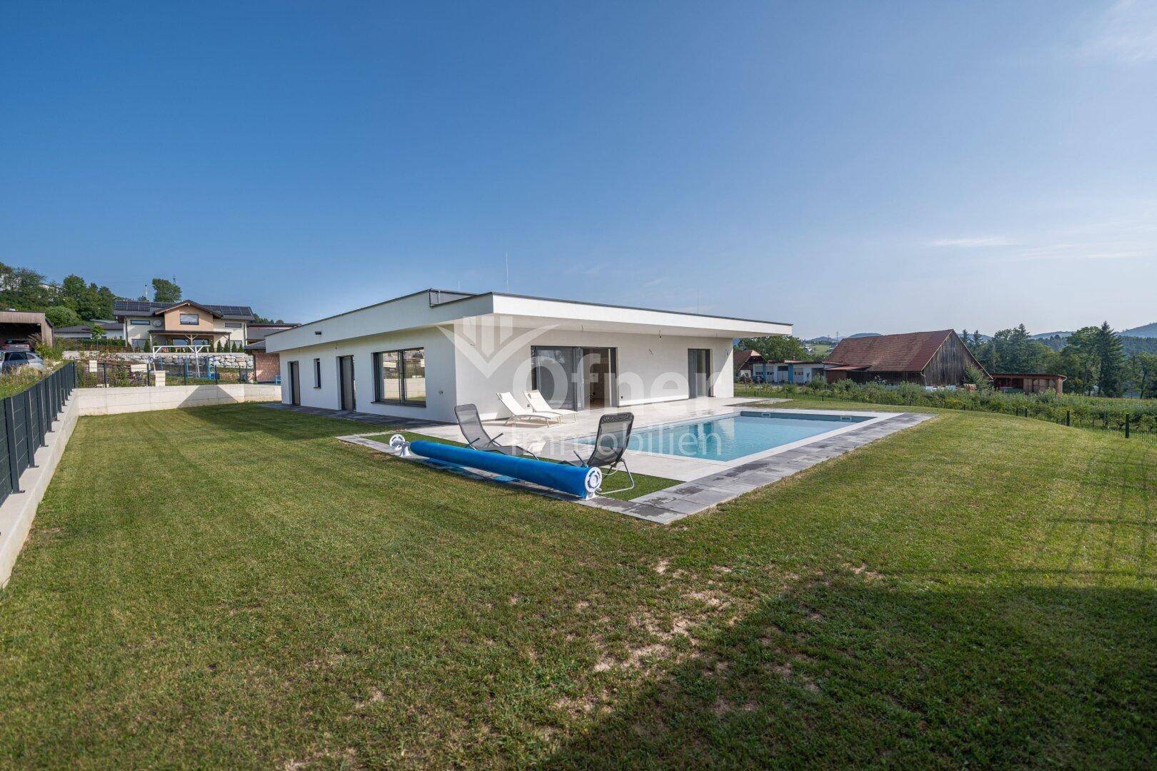 Weitläufiger Gartenbereich mit Rasen, modernem Haus und Pool unter blauem Himmel.
