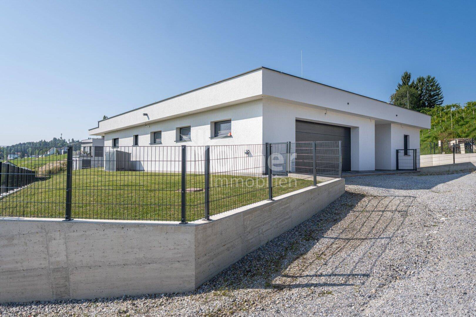 Seitenansicht des modernen Hauses mit Zaun, Garage und Zufahrt in sonniger Lage.