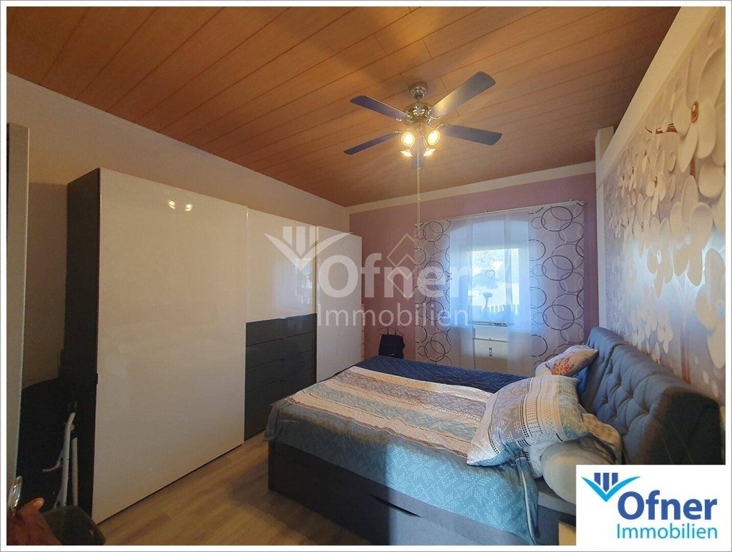 Schlafzimmer mit Holzdeckenverkleidung, Deckenventilator und großem Kleiderschrank.