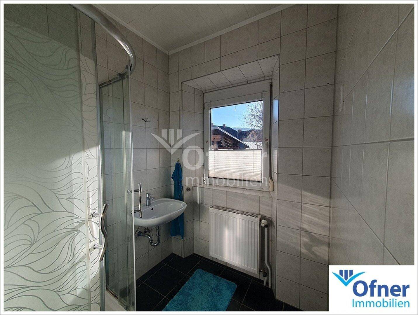 Kleines Badezimmer mit Duschkabine, Waschbecken und Fenster.
