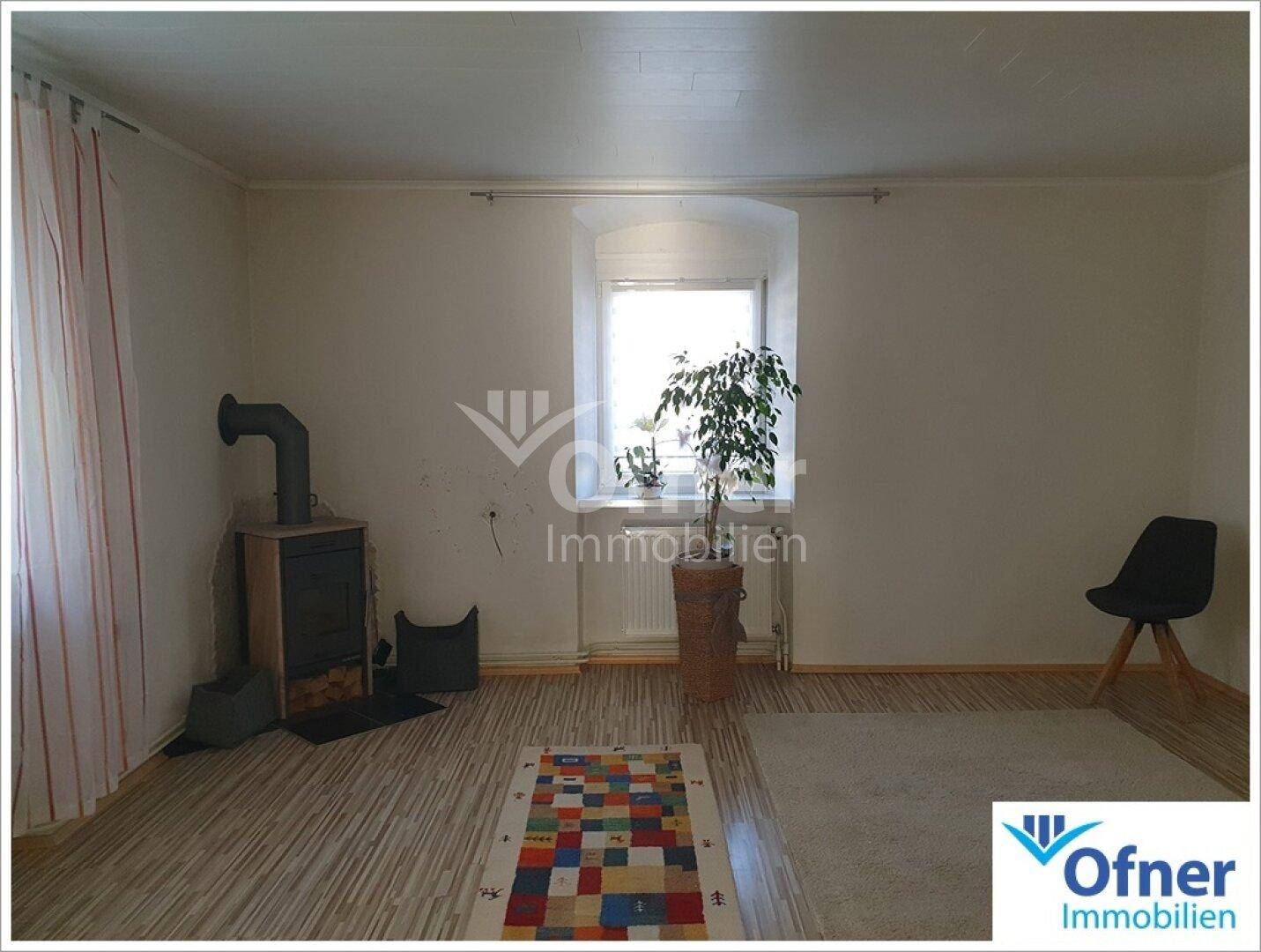 Helles Wohnzimmer mit Kaminofen, Fenster und Teppich auf Laminatboden.