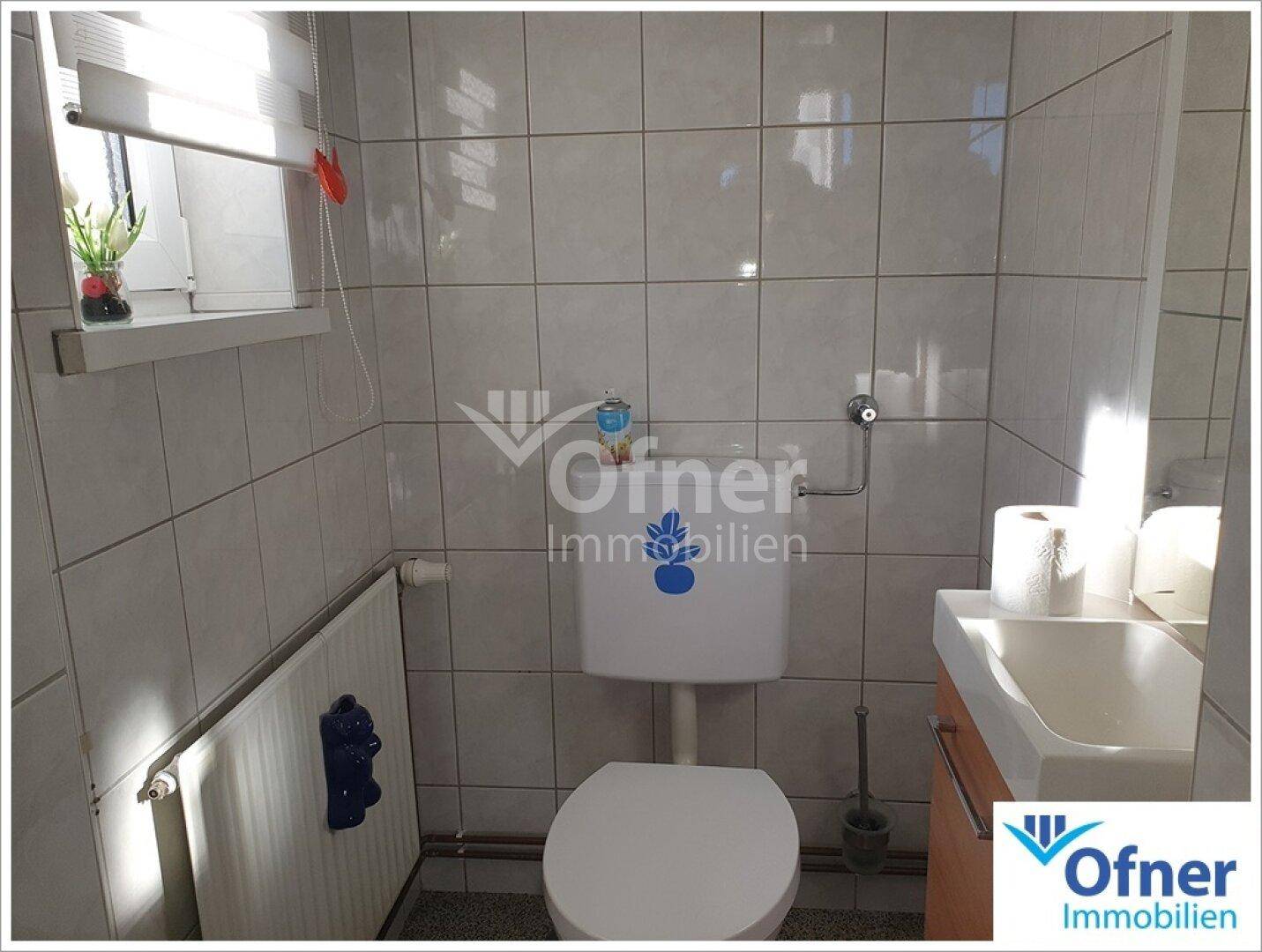 Separate Toilette mit Fenster, Wandfliesen und kleinem Waschbecken.