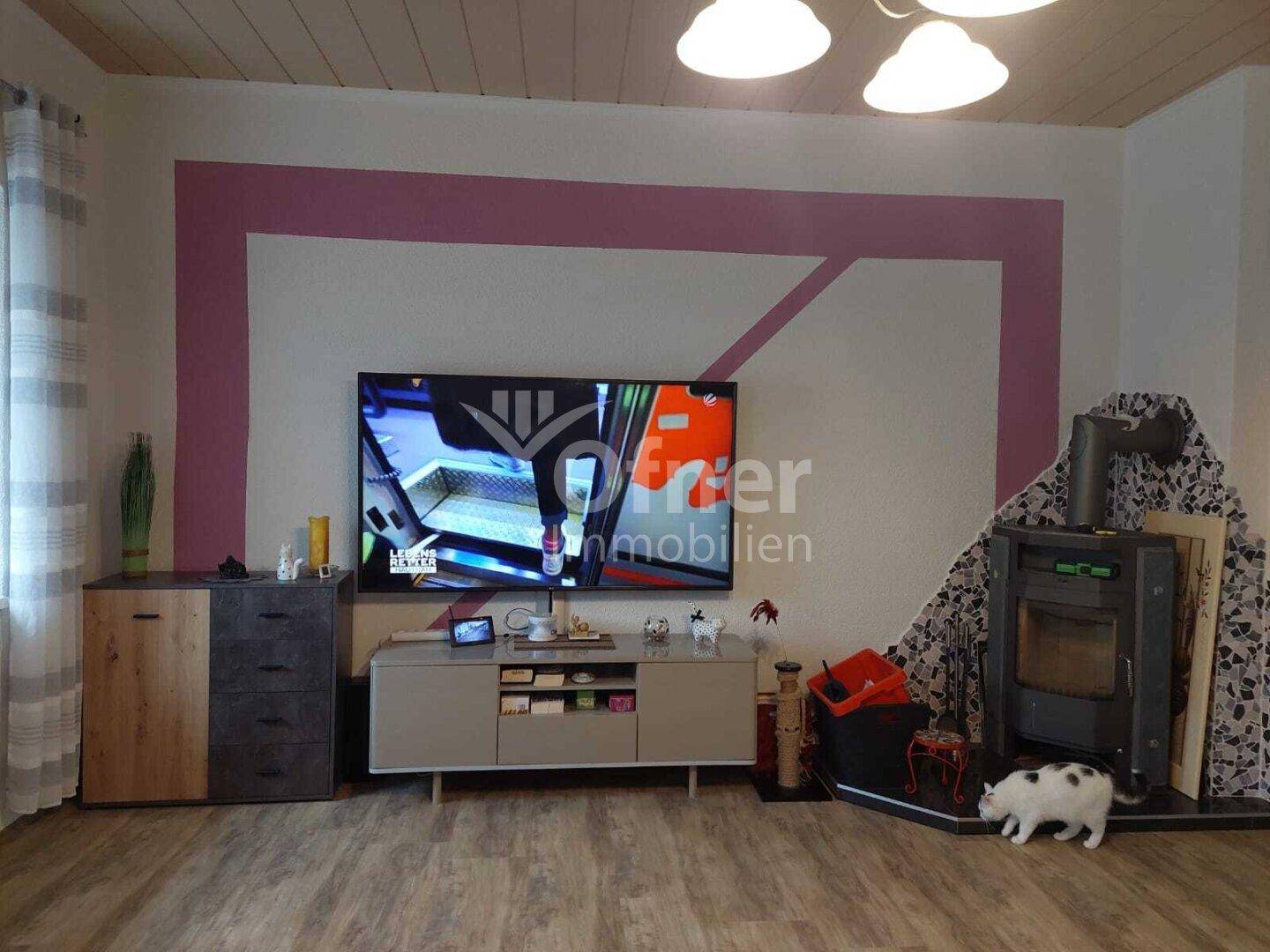 Gemütliches Wohnzimmer mit Holzboden, Kaminofen und modernem TV-Bereich.